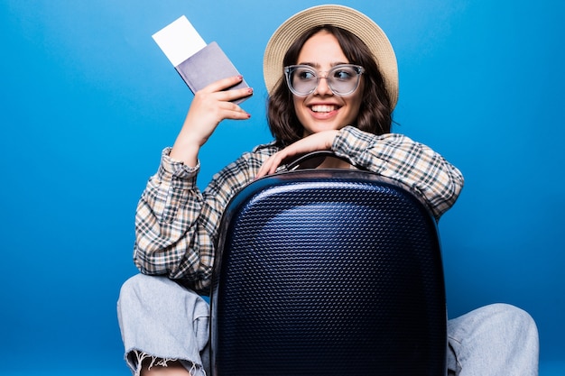 Portrait d'une jeune femme excitée vêtue de vêtements d'été tenant un passeport avec des billets de vol en se tenant debout avec une valise isolée
