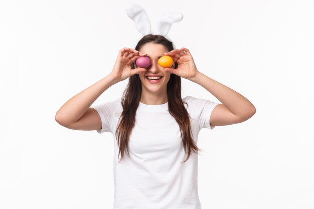Portrait jeune femme expressive porter des oreilles de lapin et le nez, tenant des oeufs colorés