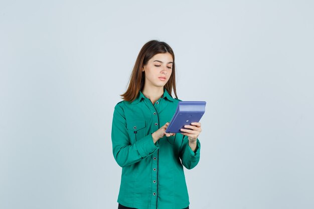 Portrait de jeune femme faisant des calculs sur la calculatrice en chemise verte et à la vue de face occupée