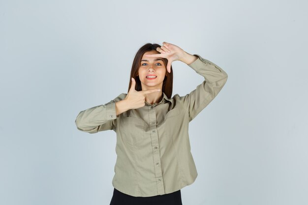 Portrait de jeune femme faisant un geste de cadre en chemise, jupe et à la vue de face heureuse