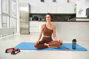 Photo gratuite portrait d'une jeune femme de fitness, une athlète féminine pratiquant le yoga à domicile, assise dans la pose du lotus avec re