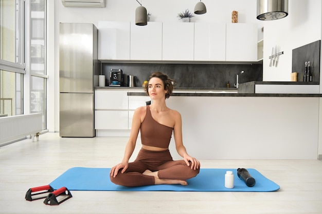 Photo gratuite portrait de jeune femme fitness athlète féminine pratique le yoga à la maison assis en posture de lotus avec re