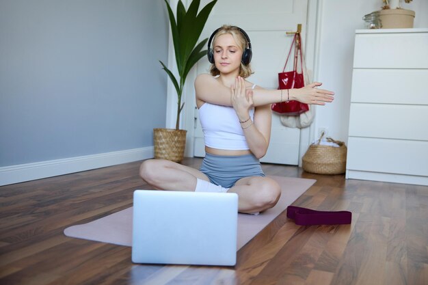 Portrait d'une jeune femme de fitness faisant des exercices d'échauffement en regardant une vidéo d'entraînement sur un ordinateur portable en train de s'étirer