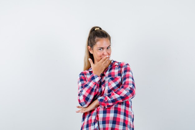 Portrait de jeune femme en gardant la main sur la bouche en chemise à carreaux et à la joyeuse vue de face