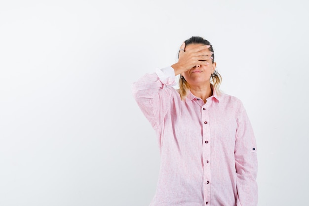 Portrait de jeune femme en gardant la main sur les yeux en chemise rose et à la vue de face impuissante