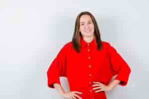 Photo gratuite portrait de jeune femme gardant les mains sur la taille en blouse rouge et à la vue de face joviale