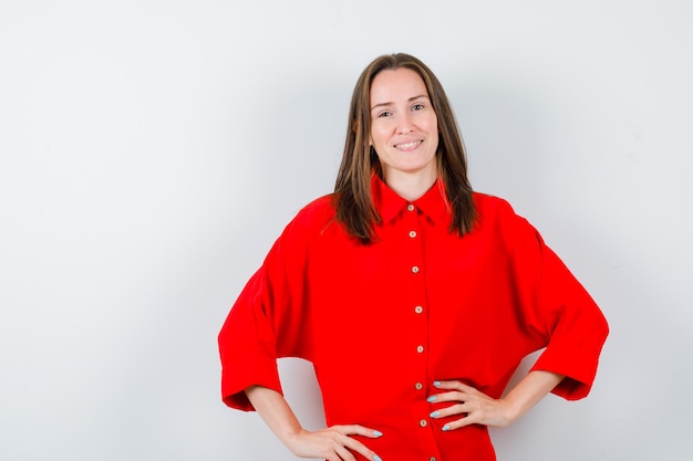 Portrait de jeune femme gardant les mains sur la taille en blouse rouge et à la vue de face joviale