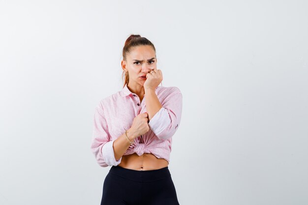 Portrait de jeune femme en gardant le poing sur la bouche en chemise, pantalon et à la vue de face effrayée