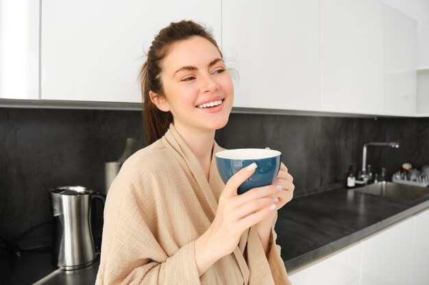 Photo gratuite portrait d'une jeune femme heureuse commence sa matinée avec une tasse de café en buvant du thé dans une tasse debout