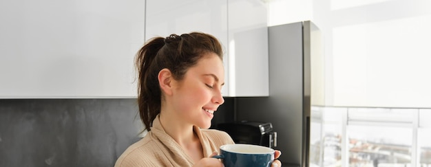 Photo gratuite portrait d'une jeune femme heureuse commence sa matinée avec une tasse de café en buvant du thé dans une tasse debout