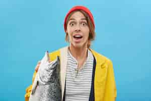 Photo gratuite portrait de jeune femme heureuse excitée debout au mur bleu blanc, tenant de gros poissons d'eau douce, se sentant joyeux et étonné. concept de personnes, passe-temps, activité, loisirs et loisirs