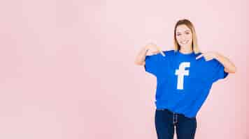 Photo gratuite portrait d'une jeune femme heureuse pointant sur son t-shirt avec l'icône facebook