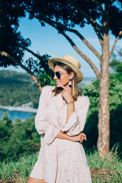 Portrait de jeune femme heureuse en robe d'été, lunettes de soleil et chapeau de paille