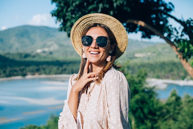 Portrait de jeune femme heureuse en robe d'été, lunettes de soleil et chapeau de paille