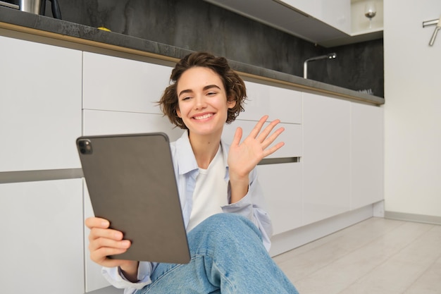 Portrait d'une jeune femme heureuse se connecte aux ondes de chat vidéo sur une tablette numérique et souriante est assise à la maison