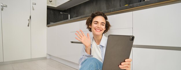 Photo gratuite portrait d'une jeune femme heureuse se connecte à des ondes de chat vidéo sur une tablette numérique et sourit assis à