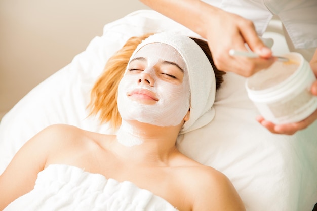 Portrait d'une jeune femme hispanique heureuse se relaxant dans un spa et recevant un soin du visage hydratant et antioxydant dans un spa