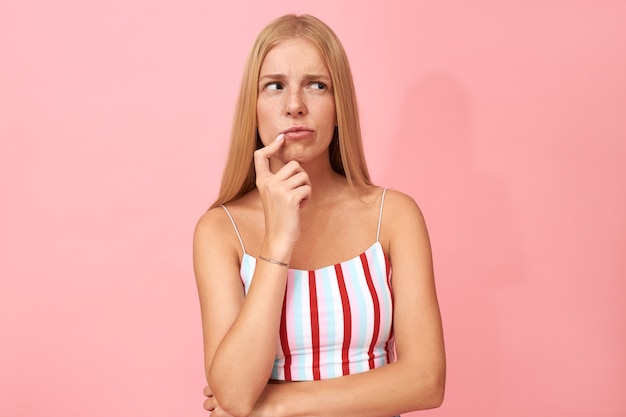 Portrait de jeune femme indécise douteuse avec des taches de rousseur toucher les lèvres et regarder ailleurs, face au dilemme, prendre une décision, choisir quoi porter pour faire la fête