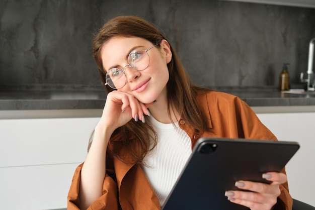 Portrait d'une jeune femme indépendante occupée assise à la maison avec une tablette numérique à lire