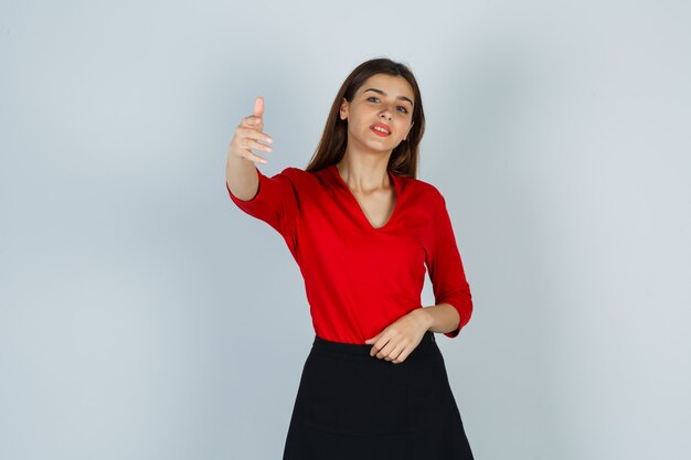 Portrait de jeune femme invitant à venir en chemisier rouge, jupe et à la jolie vue de face