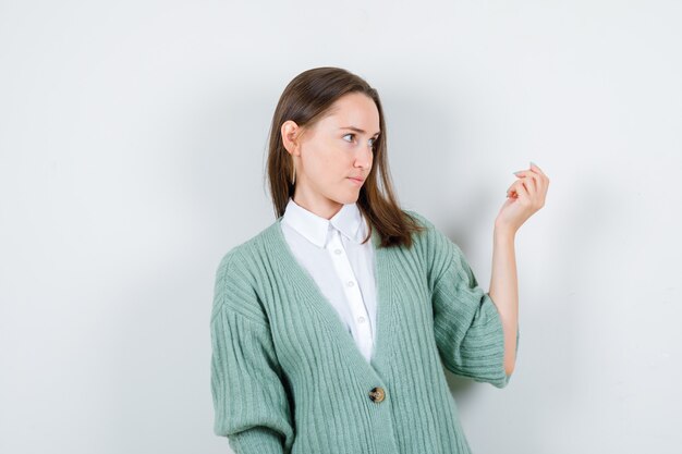 Portrait de jeune femme invitant à venir tout en regardant de côté en chemise, cardigan et regardant la vue de face focalisée