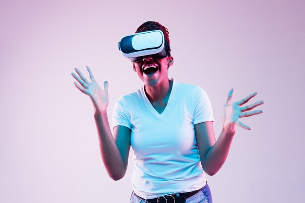 Portrait de jeune femme jouant dans des lunettes VR en néon sur gradient