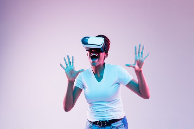 Portrait de jeune femme jouant dans des lunettes VR en néon sur gradient