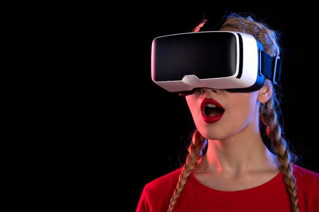 Portrait de jeune femme jouant avec enthousiasme à la réalité virtuelle sur le mur sombre