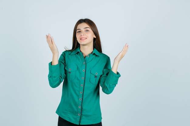 Portrait de jeune femme levant les mains tout en souriant en chemise verte et à la vue de face pleine d'espoir