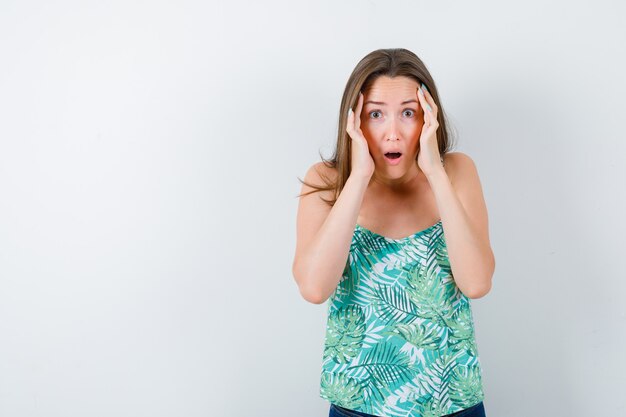 Portrait de jeune femme avec les mains sur les tempes en blouse et à la vue de face confuse