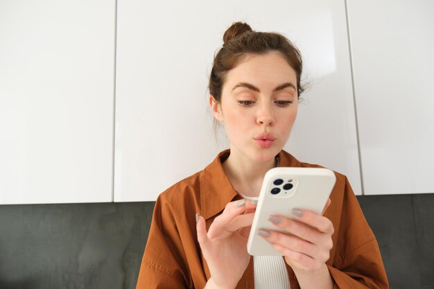 Photo gratuite portrait d'une jeune femme à la maison regardant avec intérêt l'écran d'un smartphone