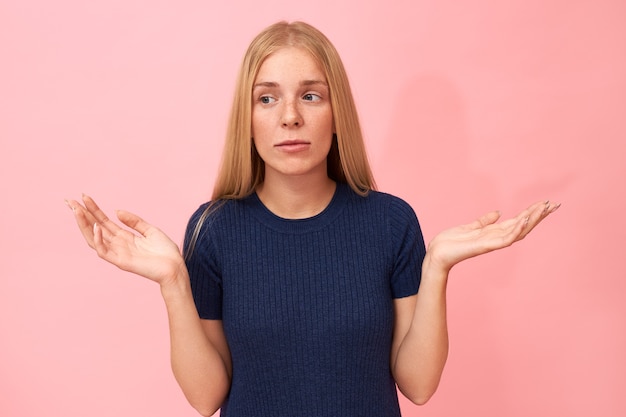 Photo gratuite portrait de jeune femme mignonne perplexe confus étant à court de mots, haussant les épaules et faisant le geste de la main, ayant une expression faciale perplexe