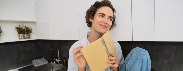 Photo gratuite portrait d'une jeune femme moderne assise dans la cuisine feuilletant des pages en lisant un journal en souriant
