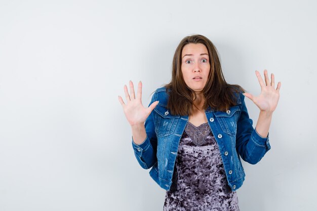 Portrait de jeune femme montrant un geste d'abandon en robe, veste en jean et à la vue de face effrayée