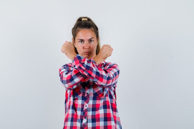 Portrait de jeune femme montrant le geste d'arrêt avec les poings croisés en chemise décontractée et à la vue de face sérieuse