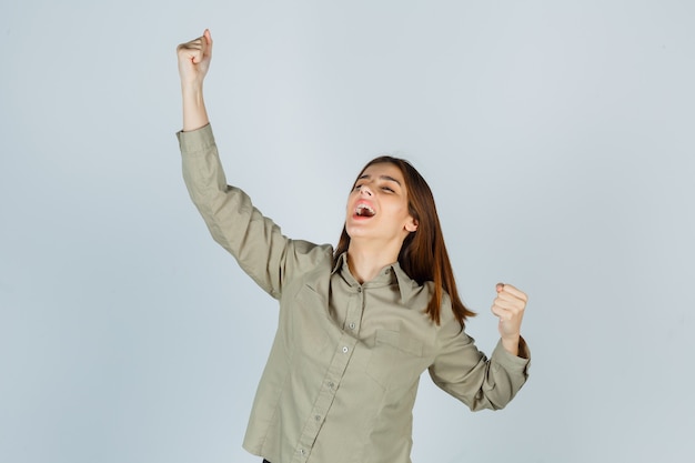Portrait de jeune femme montrant le geste du gagnant en chemise et à la vue de face heureuse
