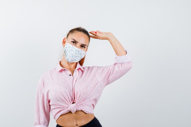 Portrait de jeune femme montrant le geste de salut en chemise, pantalon, masque et à la fière vue de face