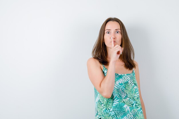 Photo gratuite portrait de jeune femme montrant un geste de silence en blouse et à la vue de face confiant