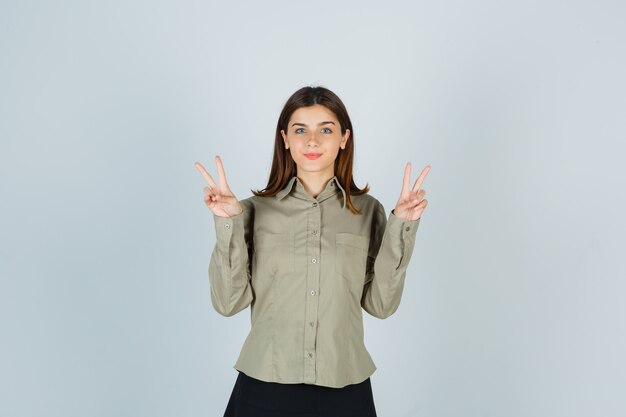 Portrait de jeune femme montrant le geste de la victoire en chemise, jupe et à la confiance