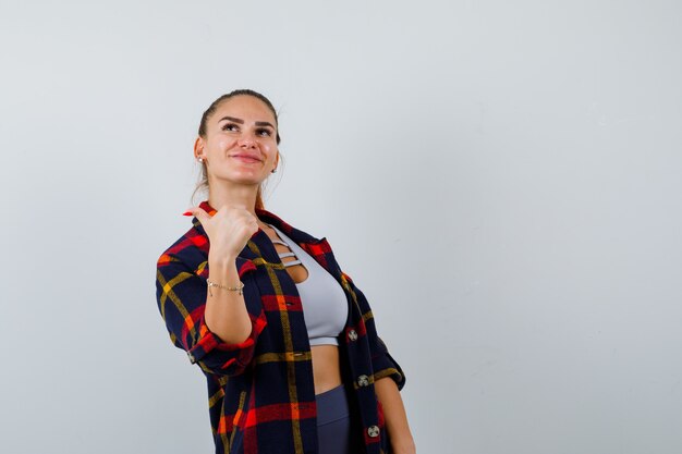 Portrait de jeune femme montrant le pouce en haut court, chemise à carreaux, pantalon et à la vue de face heureuse