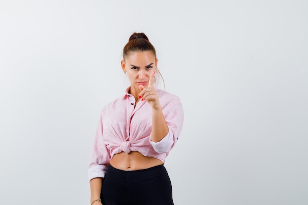 Portrait de jeune femme montrant tenir sur un geste minute en chemise, pantalon et à la vue de face sérieuse