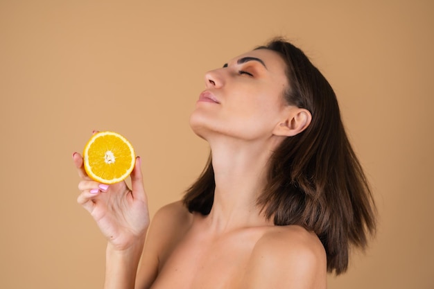 Portrait d'une jeune femme sur un mur beige avec un maquillage naturel chaud et une peau propre et lisse, tenant des cercles orange