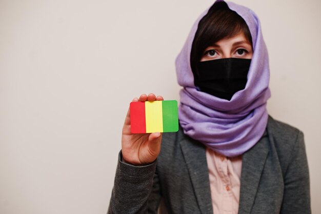 Portrait d'une jeune femme musulmane portant des vêtements de cérémonie protégeant le masque facial et le foulard hijab tenant la carte du drapeau de la Guinée sur fond isolé Concept de pays Coronavirus