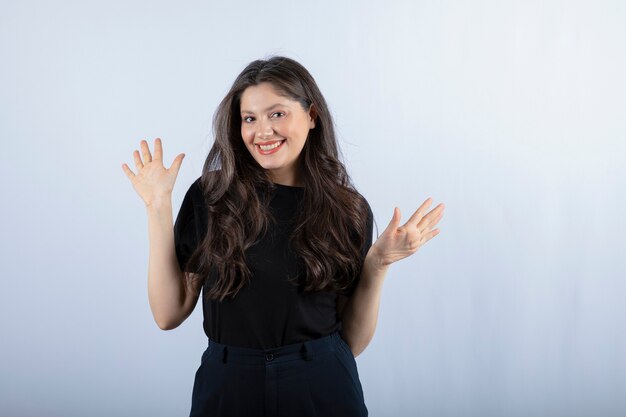 Portrait de jeune femme en noir debout sur un mur blanc.