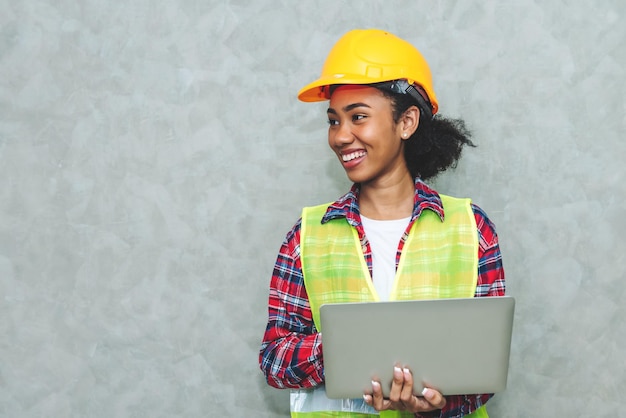 Portrait d'une jeune femme noire professionnelle ingénieur civil en architecture ouvrière portant un casque de sécurité pour travailler sur un chantier de construction ou un entrepôt en utilisant un ordinateur portable pour le travail