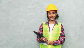 Photo gratuite portrait d'une jeune femme noire professionnelle ingénieur civil en architecture ouvrière portant un casque de sécurité pour travailler sur un chantier de construction ou un entrepôt en utilisant un ordinateur portable pour le travail