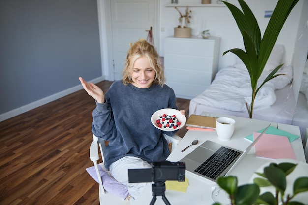 Photo gratuite portrait d'une jeune femme parlant au public enregistrant un vlog sur une caméra numérique montrant son petit déjeuner