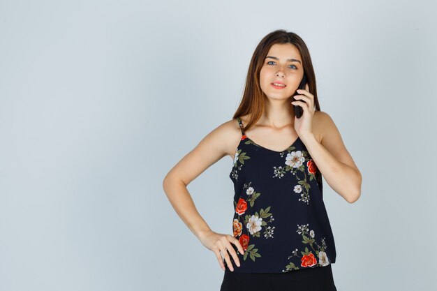Portrait de jeune femme parlant sur smartphone en blouse et regardant pensive vue de face