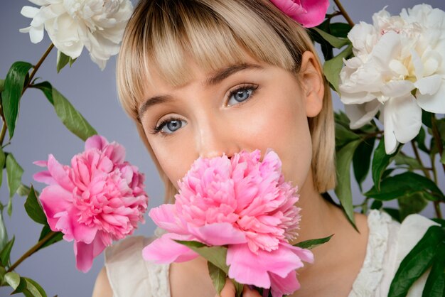 Portrait de jeune femme parmi les fleurs sur mur gris