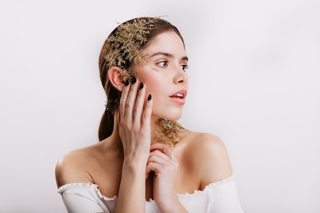 Portrait de jeune femme à la peau parfaite, posant avec de belles feuilles dans les cheveux noirs sur un mur isolé.